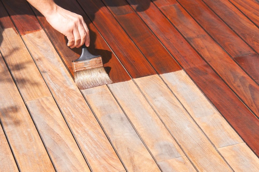 Deck Painting. Exterior wood deck renovation, annual refreshing, worker's hand is oiling terrace decking with a painting brush after sanding.