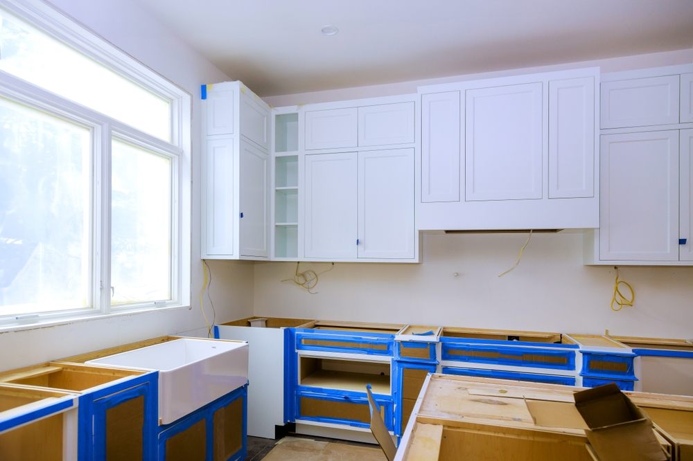 Cabinet Painting. New kitchen construction underway featuring white cabinets house sink along with unfinished cabinetry blue masking tape for protection.