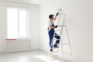 Residential Painting. Handyman painting wall with roller brush indoors, space for text. Professional construction tools.